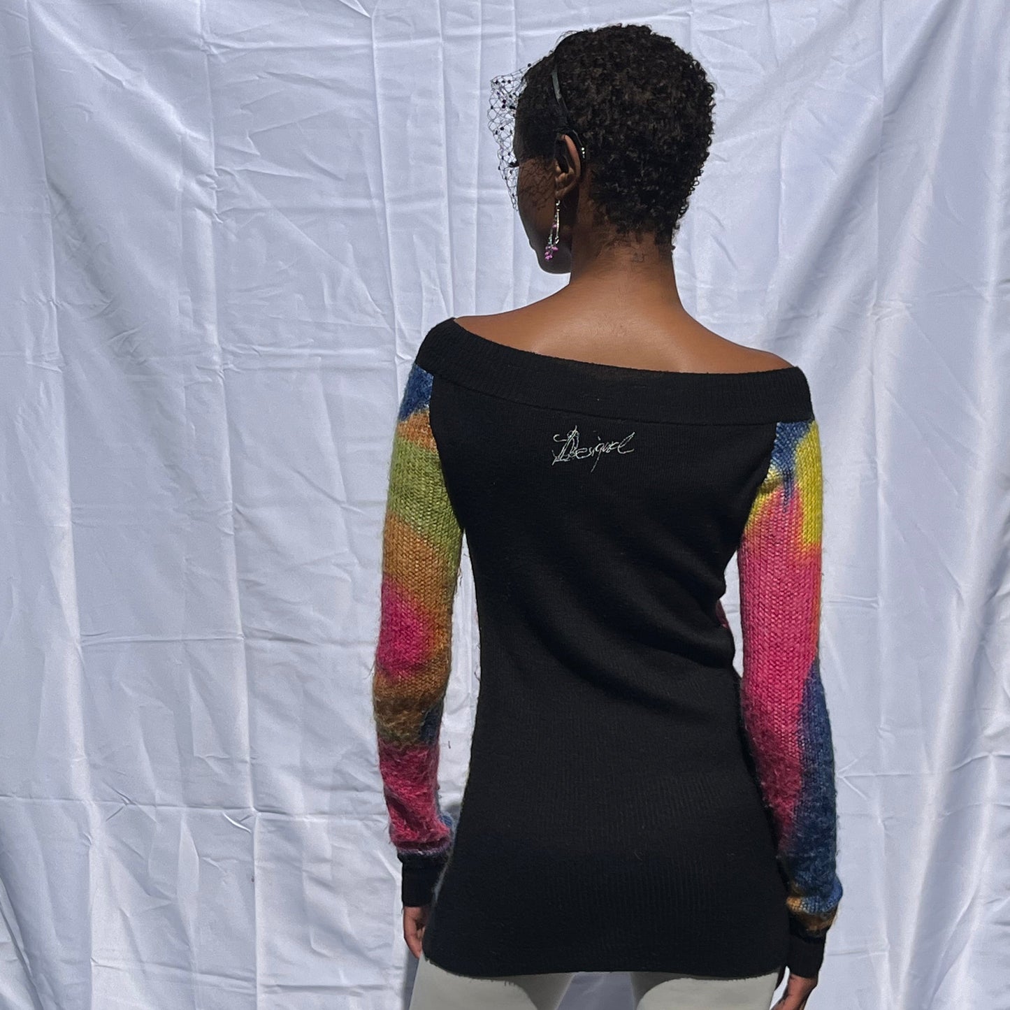 Person wearing a black shirt with colorful sleeves against a white backdrop