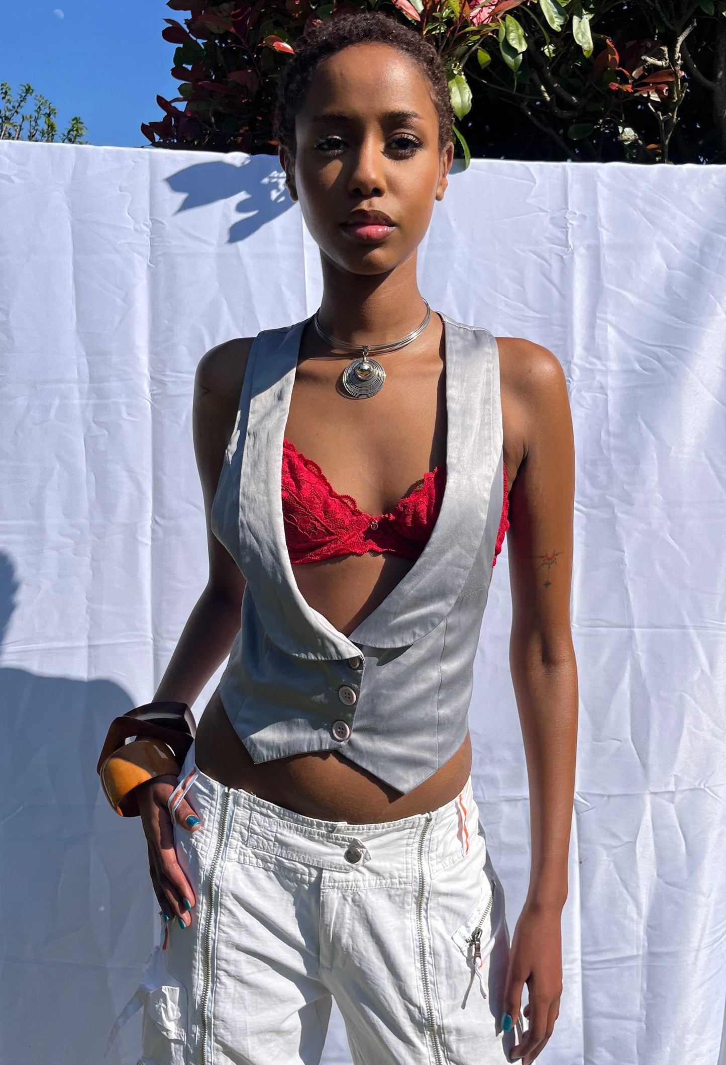 Person wearing a metallic top and white pants on a white sheet outdoors