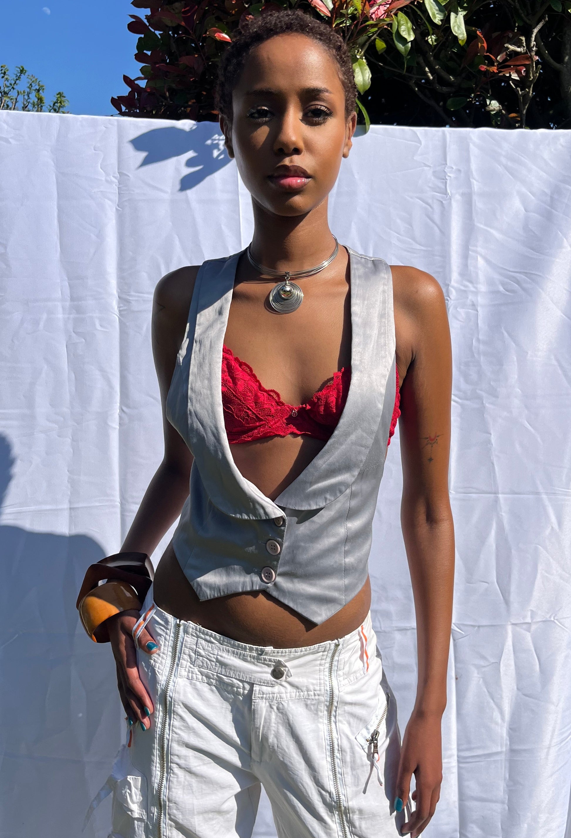 Person wearing a metallic top and white pants on a white sheet outdoors