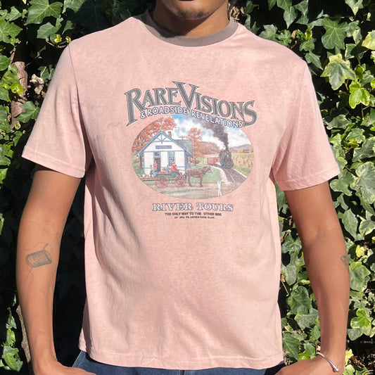 Person wearing a vintage pink t-shirt with a colorful graphic and text, standing among green foliage.